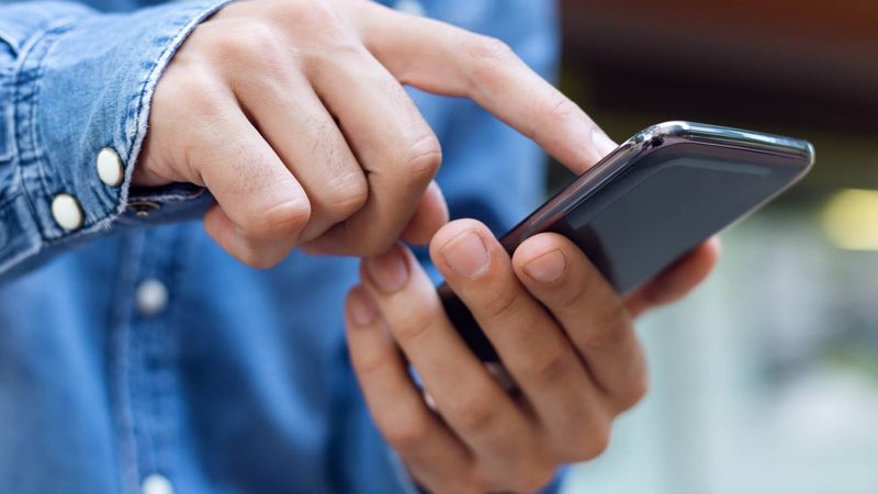 человек в синей джинсовой рубашке касается пальцем сенсорный телефон
