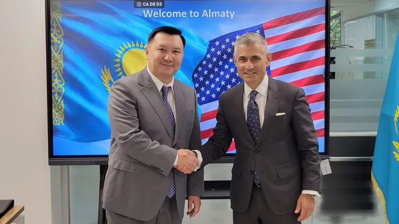 Представитель Almatyinvest и представитель госдепа США пожимают друг другу руки на фоне совместных флагов двух стран