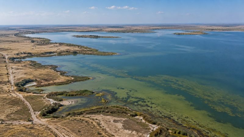 Вид сверху на накопитель Сорбулак с водой, береговой линией и степной местностью вокруг