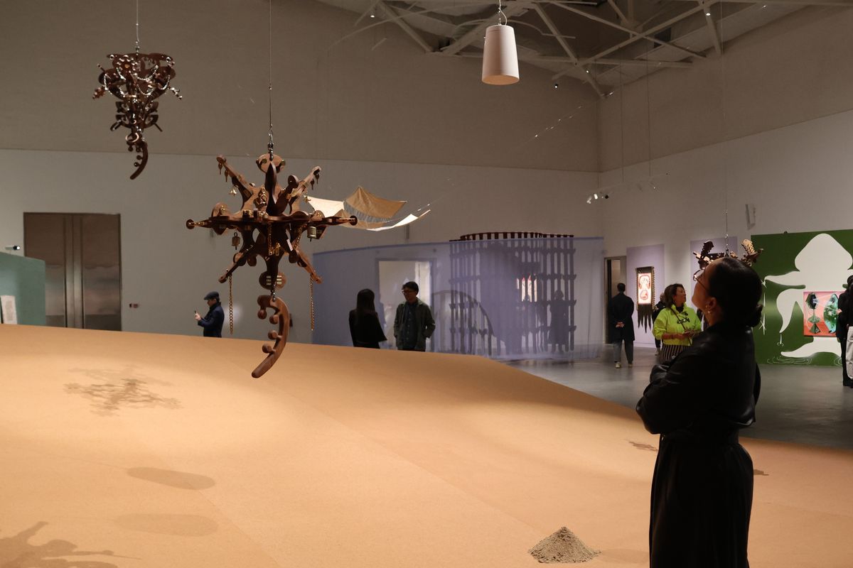 Подвесные деревянные скульптуры с колокольчиками над песочной инсталляцией в выставочном зале &laquo;Целинного&raquo;